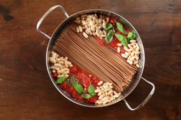 Skillet of Einkorn whole grain linguine cooking in marinara sauce with cannellini beans and fresh basil on a wooden countertop