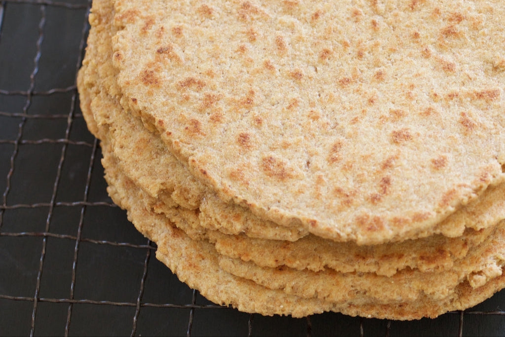 Close-up of stacked 100 percent whole-grain Einkorn flatbreads showing toasted spots and coarse whole-grain texture on a dark cooling rack