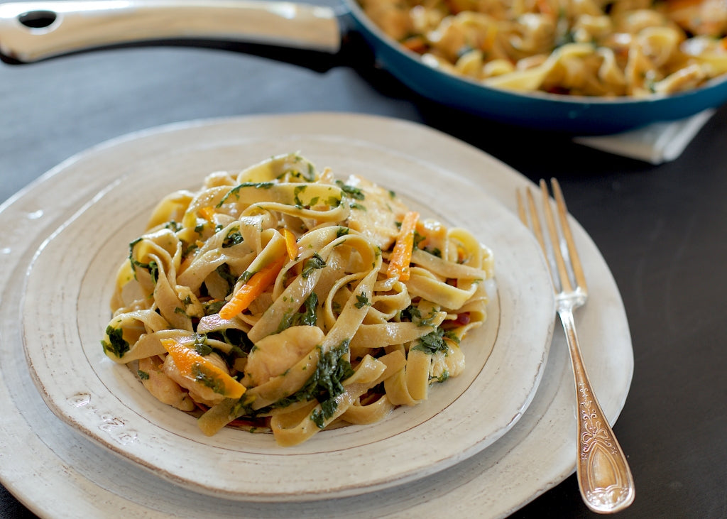 Tagliatelle with Prosecco chicken and rainbow chard tossed with heirloom carrots on a ceramic plate with a fork and skillet in the background