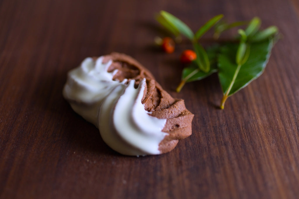 Close-up of Italian chocolate Esse cookie showing a piped two-tone swirl and ridged edge on a wooden surface with green bay leaves