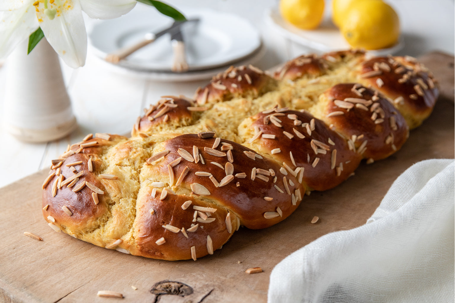 Close up of braided Einkorn Easter bread showcasing glossy golden crust, slivered almonds, and soft crumb on a wooden cutting board