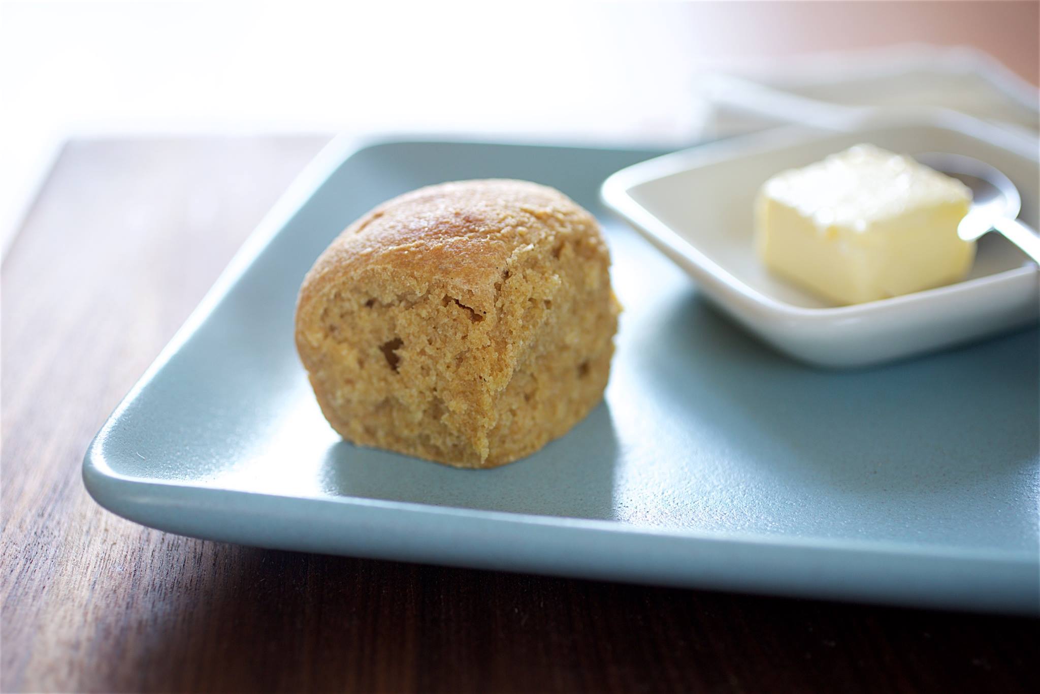Single whole-grain einkorn dinner roll on a blue plate with a small dish of butter
