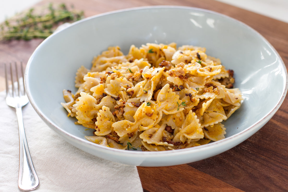 Gluten-free farfalle tossed with roasted butternut squash and crumbled sausage in a light blue bowl on a wooden board