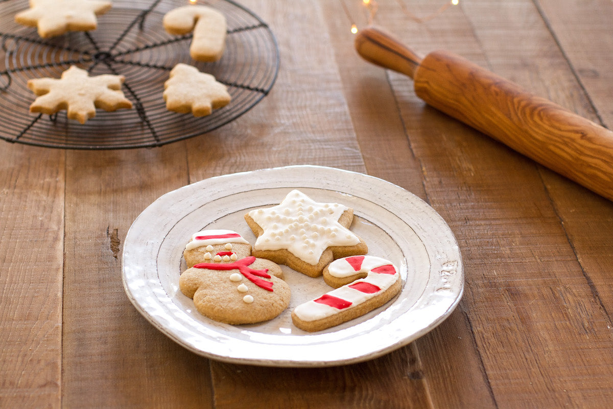 Decorated Einkorn sugar cookies (snowman, star, candy cane) on a plate with rolling pin and cooling rack in background