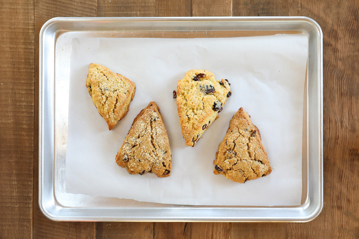 Top-down of four Einkorn orange cranberry scones showing golden-brown crust and visible cranberries on a parchment-lined baking sheet