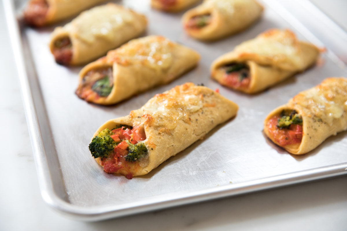 Baked Einkorn pizza roll-ups on a rimmed baking sheet with melted cheese and broccoli and tomato filling