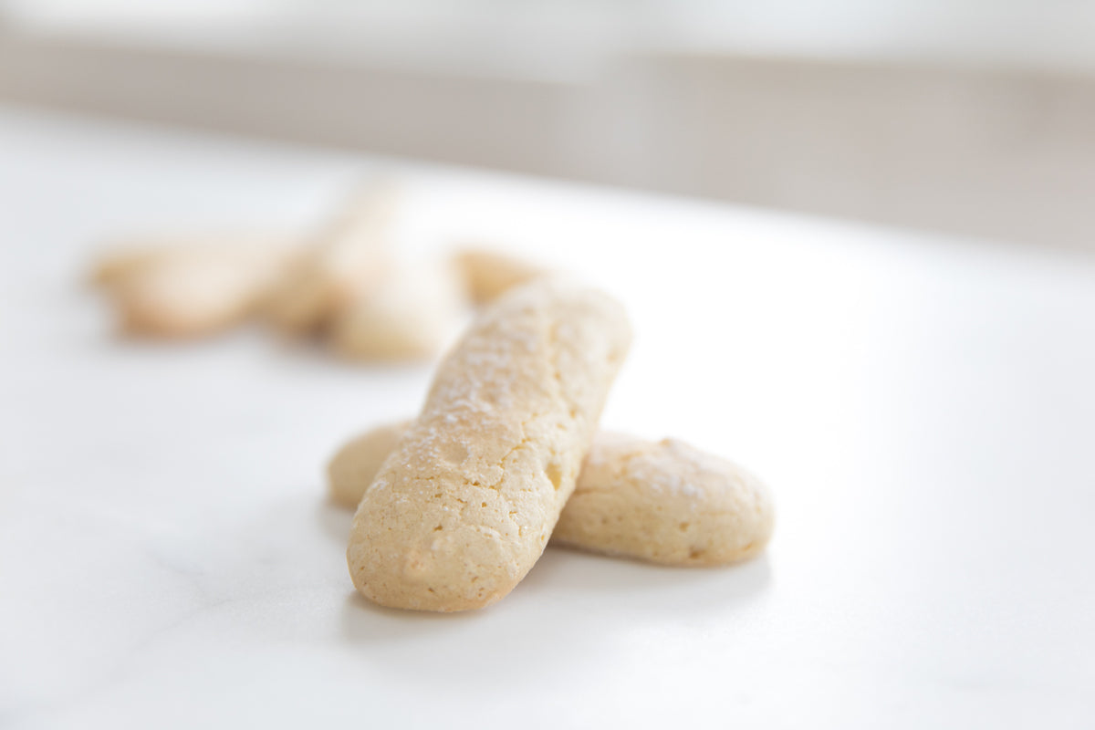 Close-up of Einkorn ladyfingers showcasing airy texture and light powdered sugar on a white marble surface