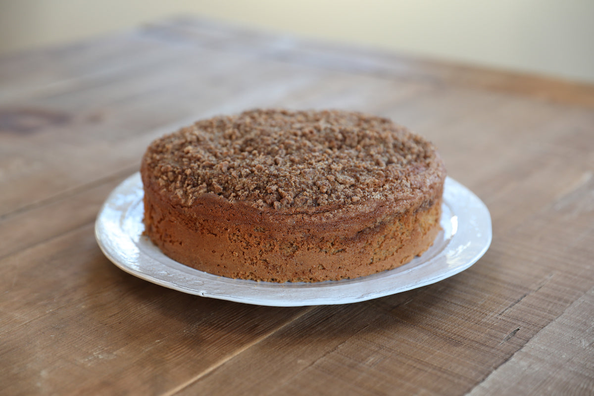 Three-quarter view of Einkorn sour cream coffee cake with cinnamon streusel topping on a white plate on a wooden table