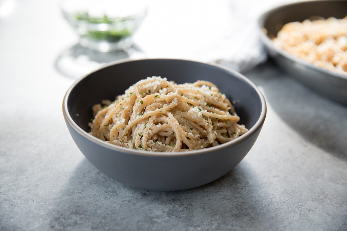 Einkorn spaghetti tossed with pan-roasted cauliflower and grated cheese served in a gray bowl on a light tabletop