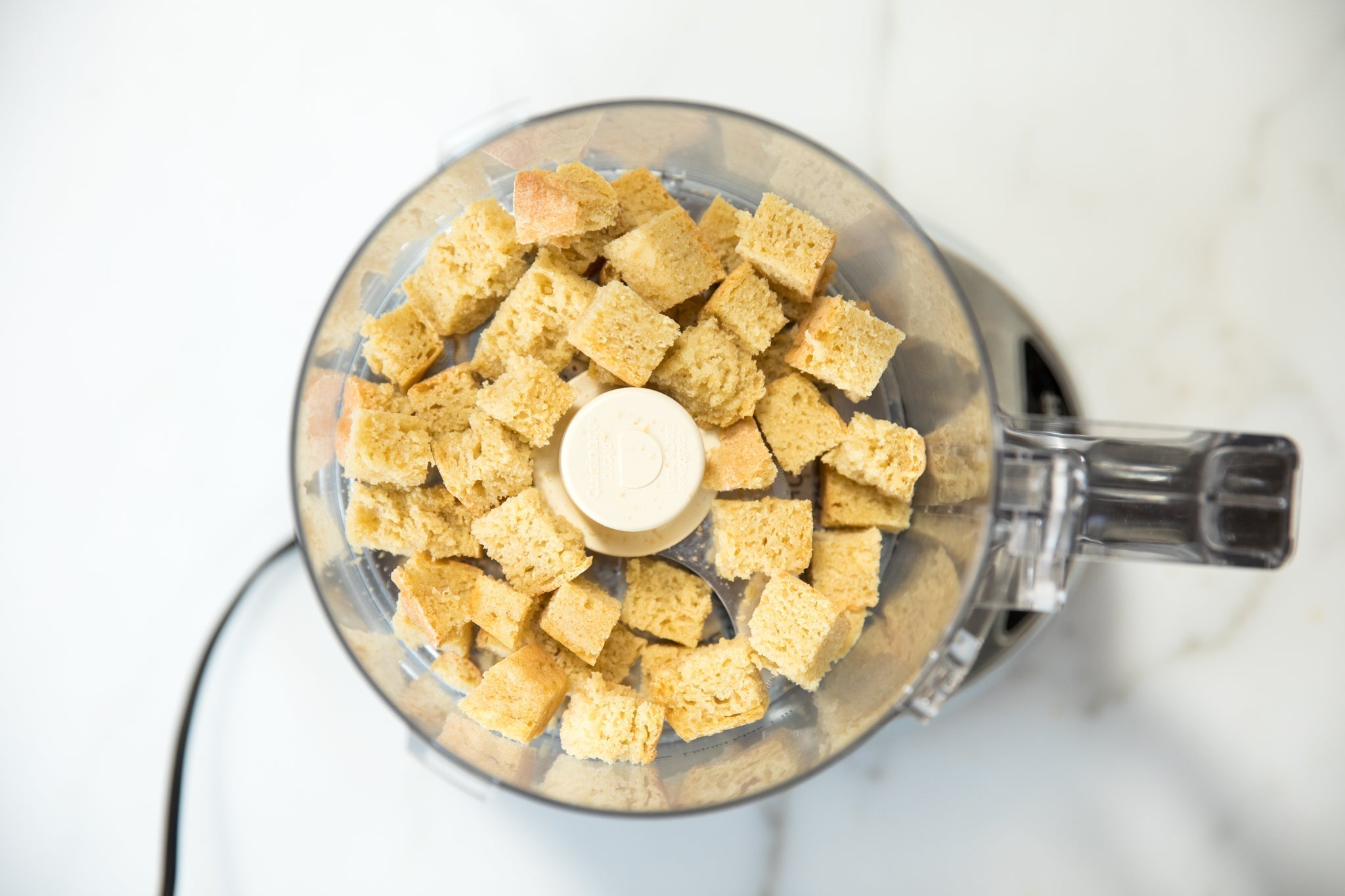 Top-down view of cubed einkorn bread in a food processor ready to be pulsed into breadcrumbs