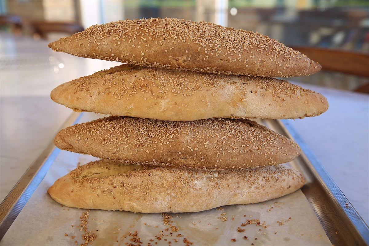 Side view of four stacked crusty Einkorn Italian bread loaves showcasing golden crust and sesame topping on a baking sheet