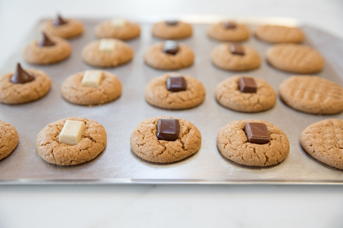 Einkorn peanut butter blossom cookies cooling on a baking sheet, each topped with a square of chocolate