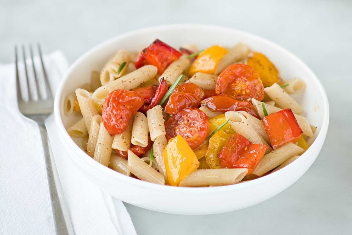 Bowl of Einkorn penne tossed with oven-roasted cherry tomatoes and red and yellow peppers on a light tabletop