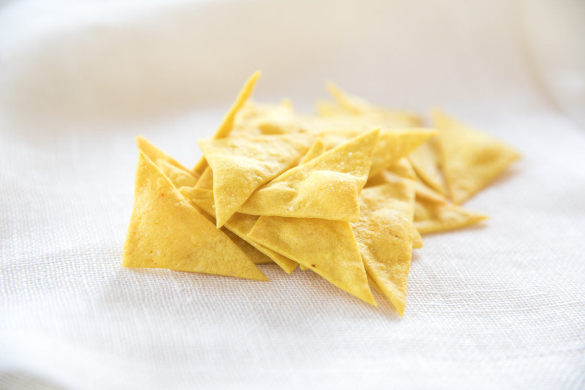 Close-up of homemade olive oil chips showing triangular baked shape and crisp texture on a white linen cloth