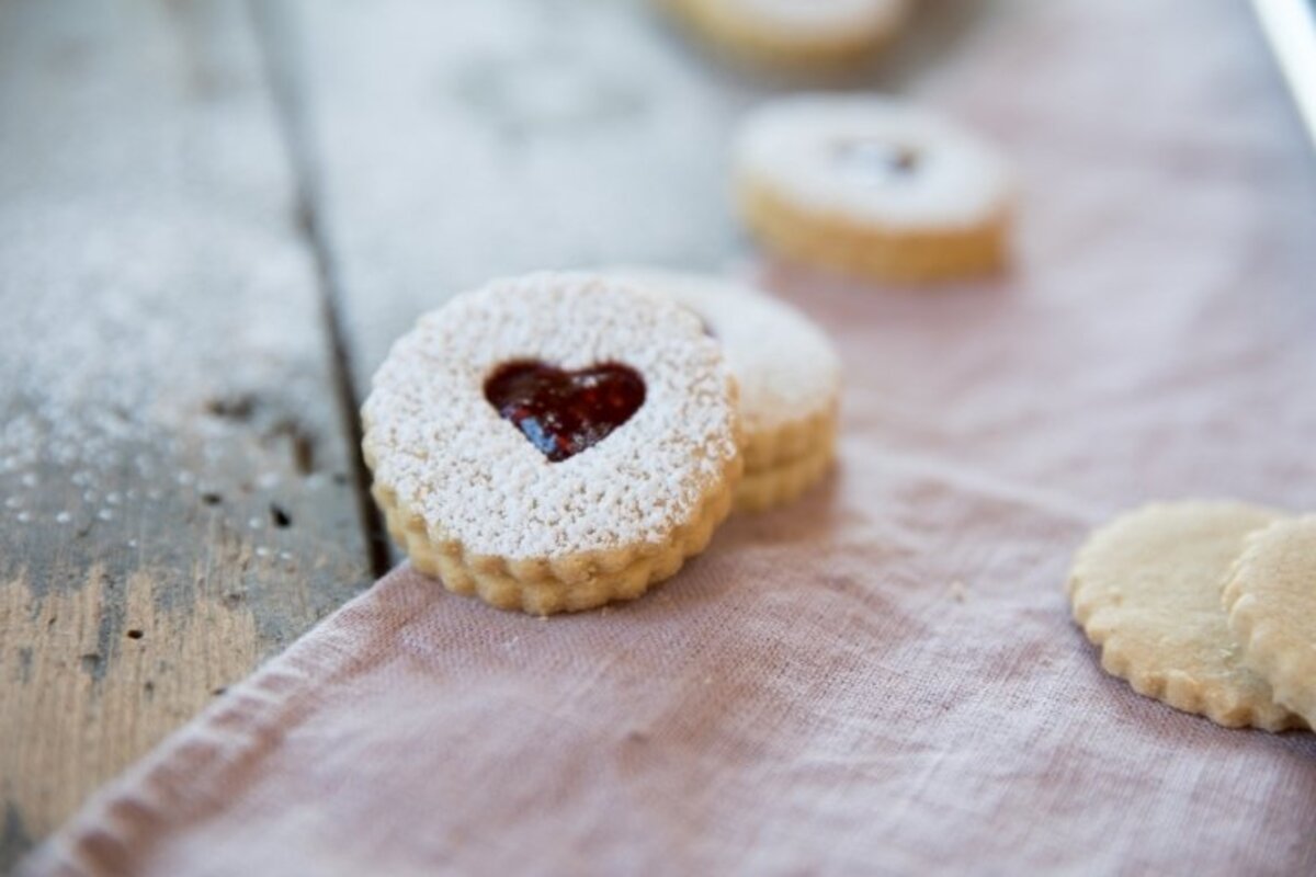 Close-up of Einkorn Linzer cookie showing heart-shaped jam center and powdered sugar on pink linen on wooden table
