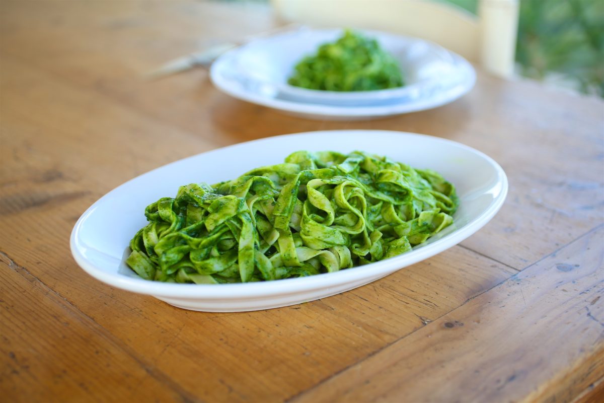 Two plates of tagliatelle tossed in bright green kale pesto on a rustic wooden table