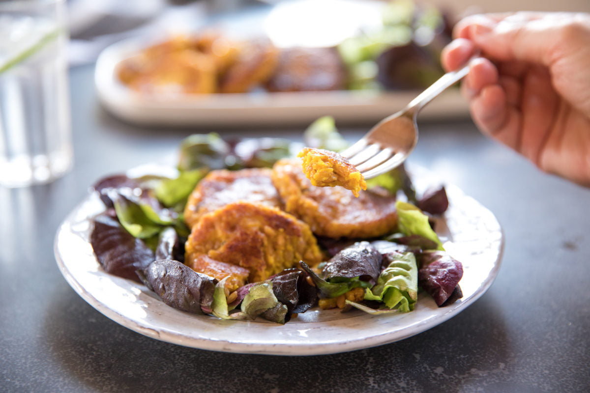 Einkorn squash croquettes on mixed salad greens, a hand lifting a croquette with a fork