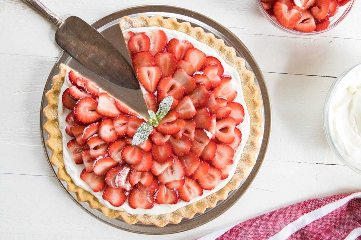 Overhead view of an Einkorn sugar cookie fruit pizza topped with sliced strawberries, a slice being lifted with a pie server