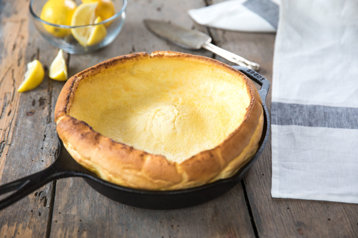 Einkorn Dutch baby pancake puffed and golden in a cast-iron skillet with lemon wedges and linen napkin on a wooden table