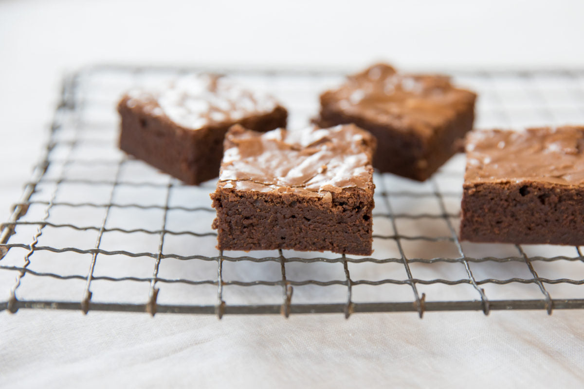 Front view of fudgy Einkorn mocha brownies showing crackled top and dense interior on a wire cooling rack with white cloth background