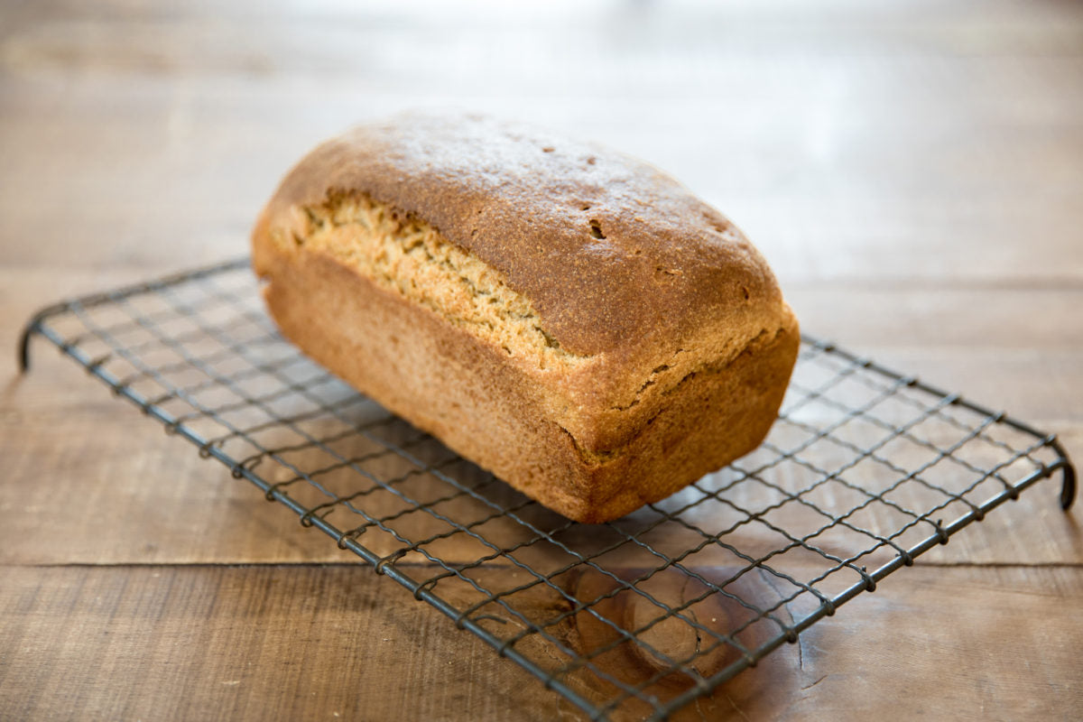 Angled view of Einkorn sourdough sandwich loaf with golden crust on a cooling rack over a wooden table