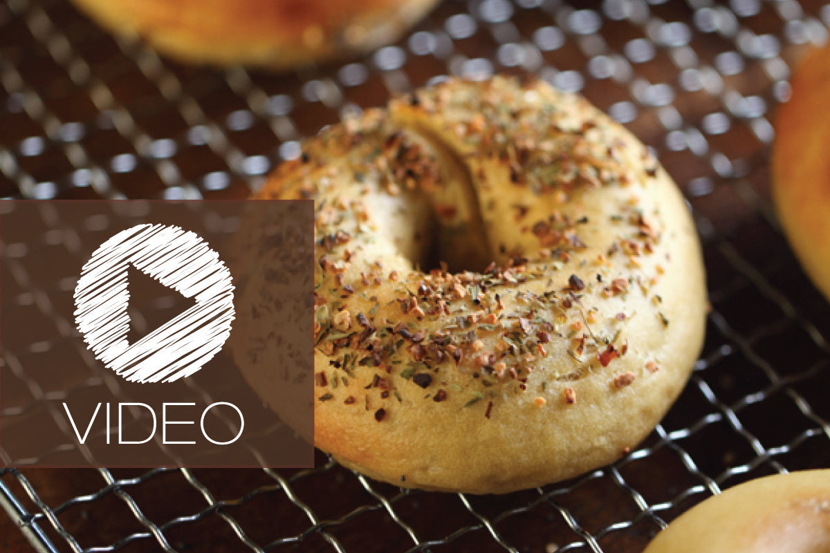 Einkorn sourdough bagel on a cooling rack with a play icon and large ‘VIDEO’ overlay