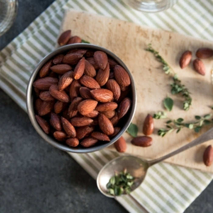Top-down view of olive oil and sea salt roasted almonds in a metal bowl showcasing the toasted brown coating on a striped napkin and wooden board
