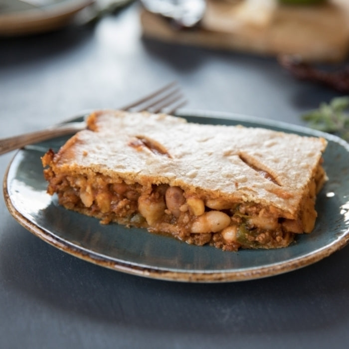 Close-up of a slice of Einkorn chili con carne pot pie showing four bean filling and golden crust on a blue ceramic plate