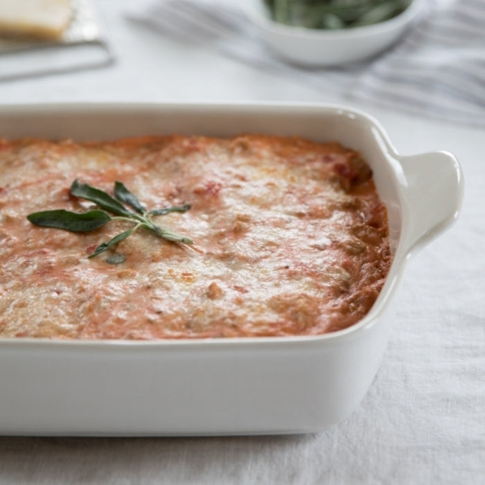 Gluten-free butternut squash stuffed manicotti baked in a white rectangular dish, topped with melted cheese and a sage sprig
