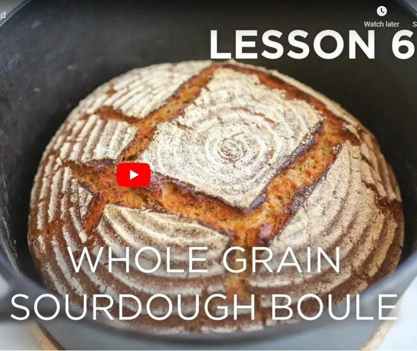 Top-down view of a whole-grain einkorn sourdough boule with scored crust and flour-ring pattern in a black Dutch oven