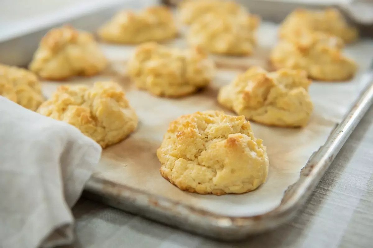 Three-quarter view of Einkorn butter drop biscuits showing golden, flaky tops on a parchment-lined baking sheet
