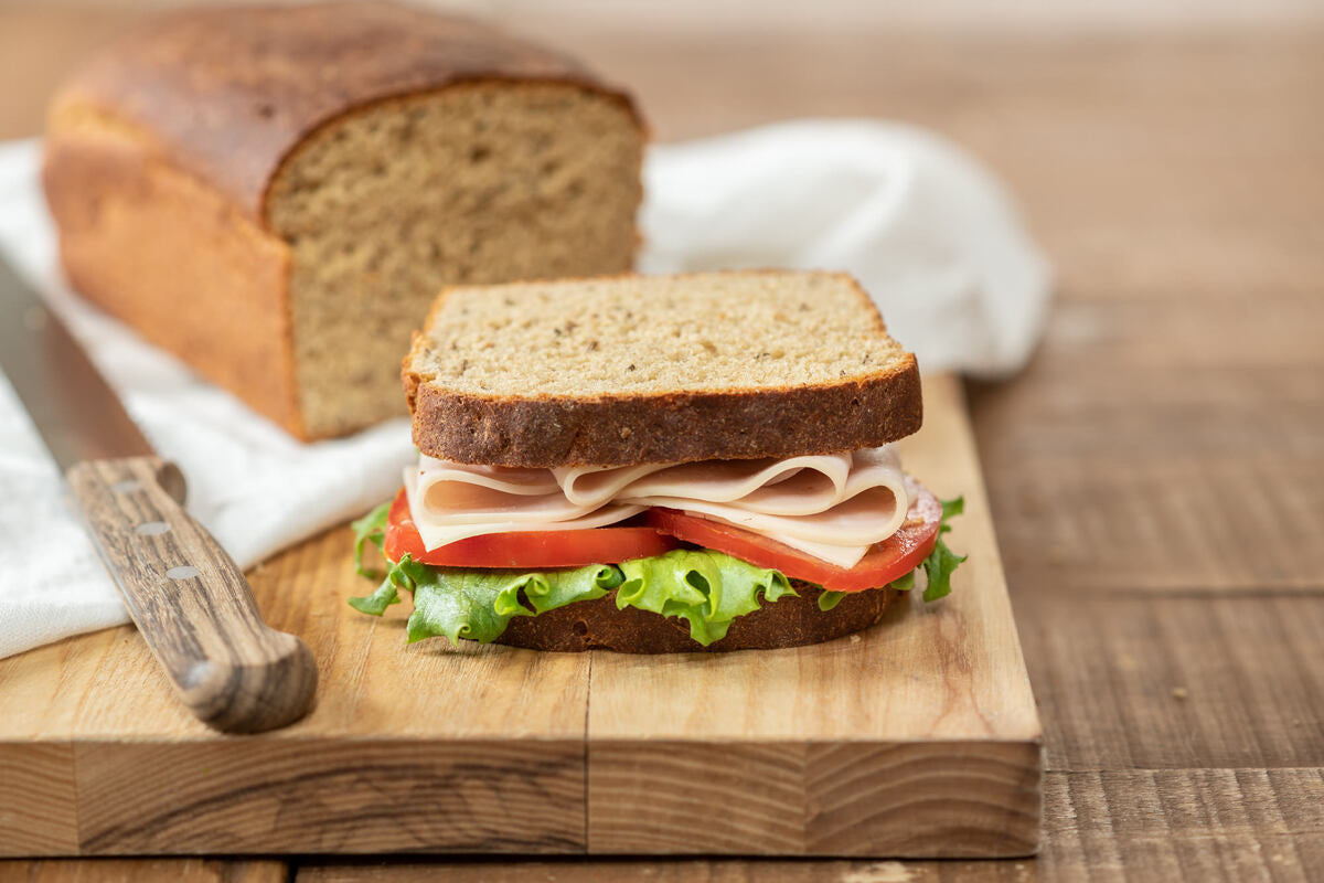 Sliced Einkorn sourdough rye sandwich with turkey, tomato, and lettuce on a wooden cutting board with loaf and knife in the background