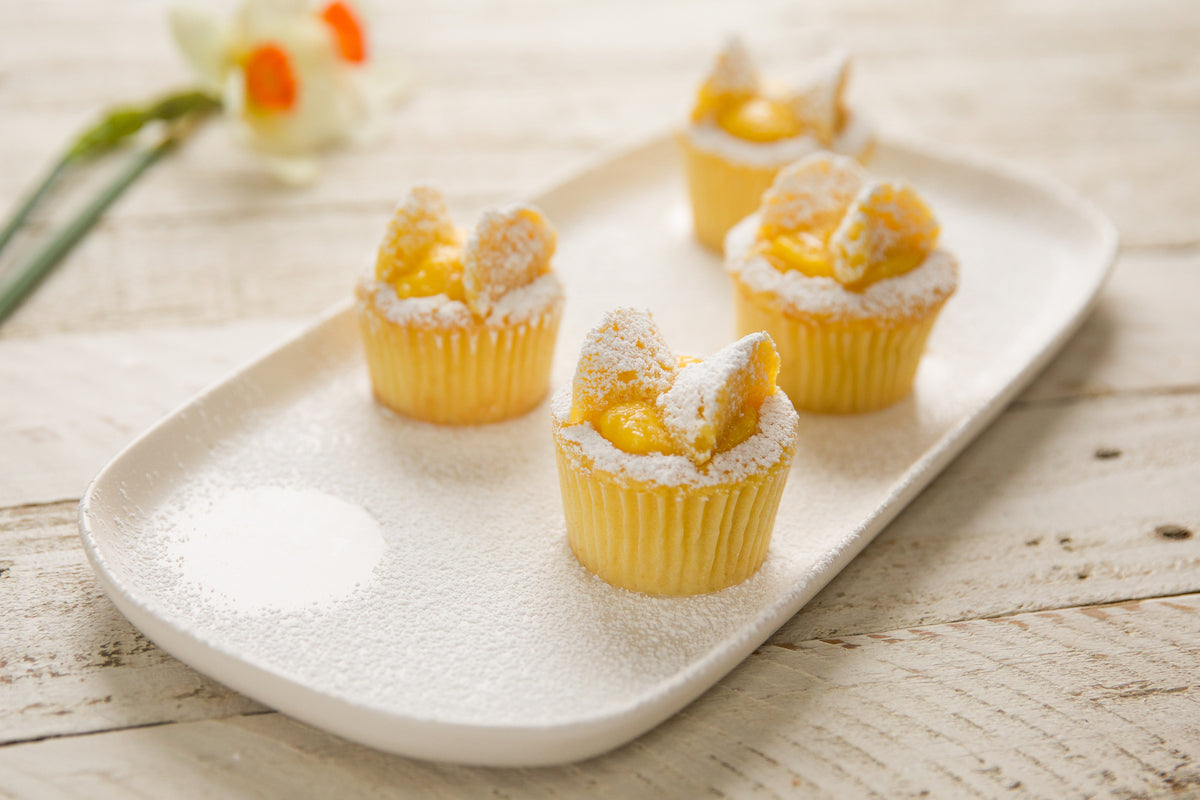 Four Einkorn lemon cupcakes with lemon curd centers, dusted with powdered sugar on a white oval platter on a rustic wooden table