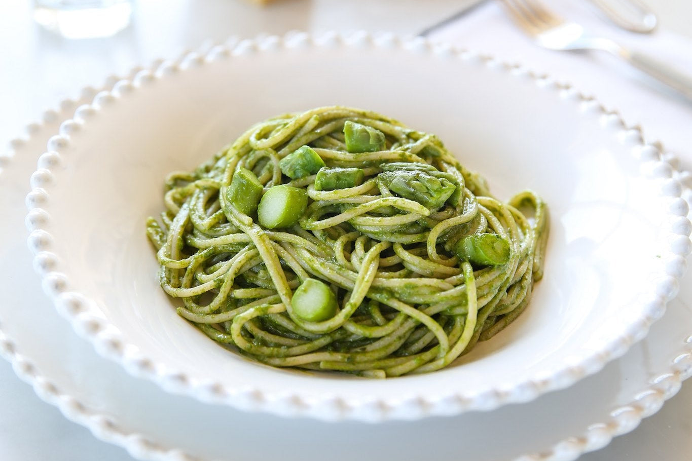 Plate of gluten free spaghetti tossed in asparagus pesto with asparagus pieces in a white scalloped bowl