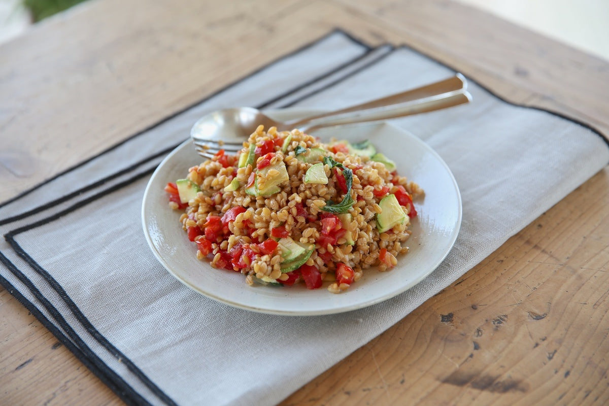 Einkorn wheat berry salad with tomatoes and avocado served on a white plate over a linen napkin on a wooden table