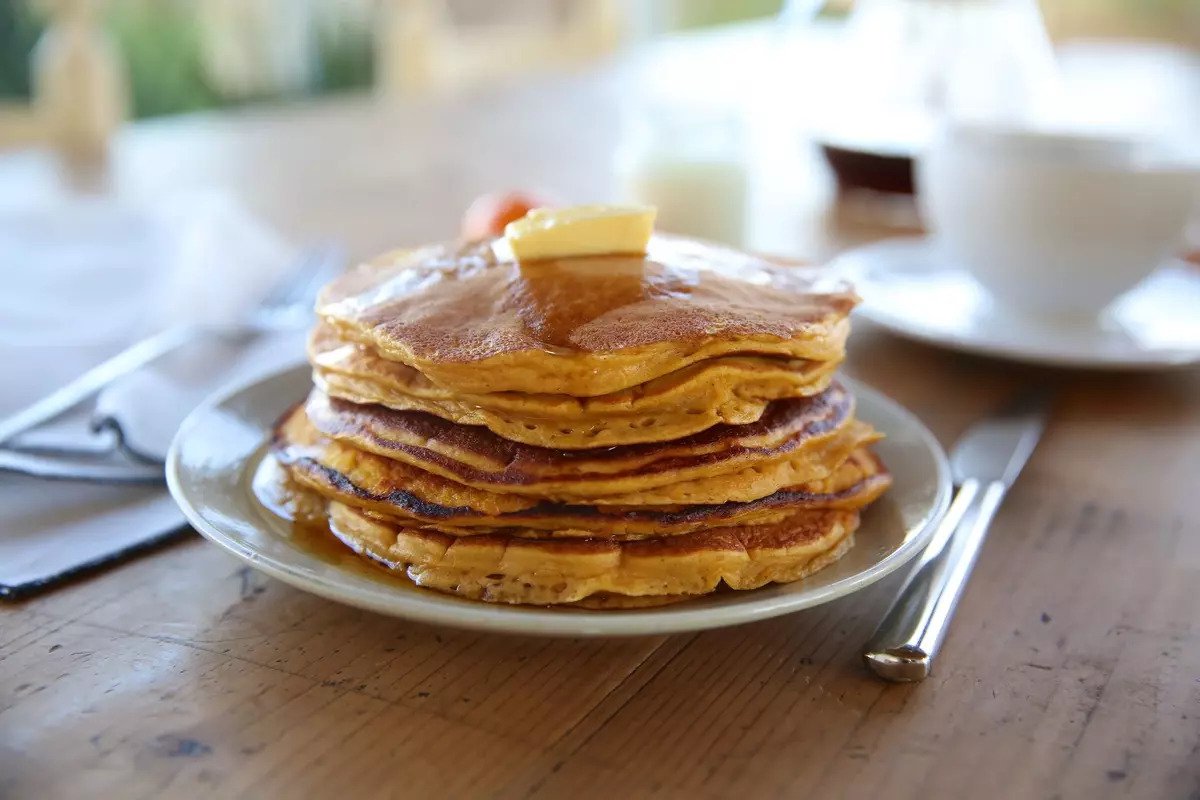 Stack of Einkorn pumpkin pancakes topped with butter and maple syrup on a wooden breakfast table