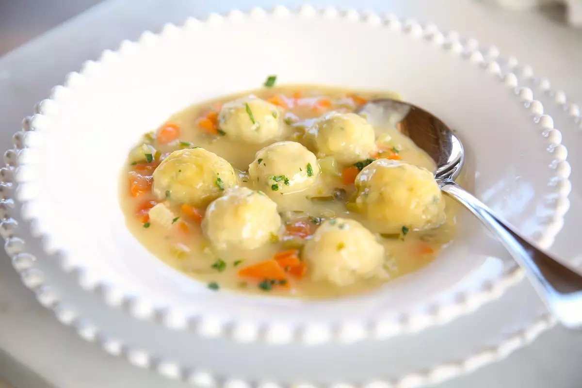 Bowl of Einkorn chicken and dumplings in creamy broth with carrots and parsley, served in a white beaded rim bowl with a spoon