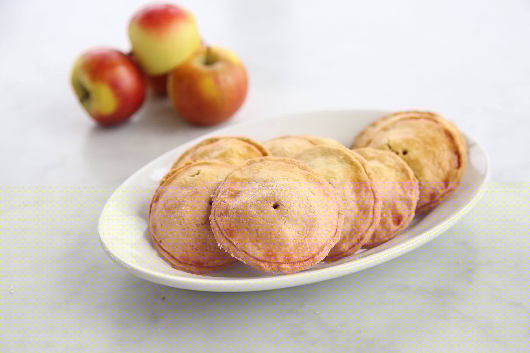 Angled top view of six Einkorn apple hand pies showing golden flaky crusts and small vent holes on a white plate