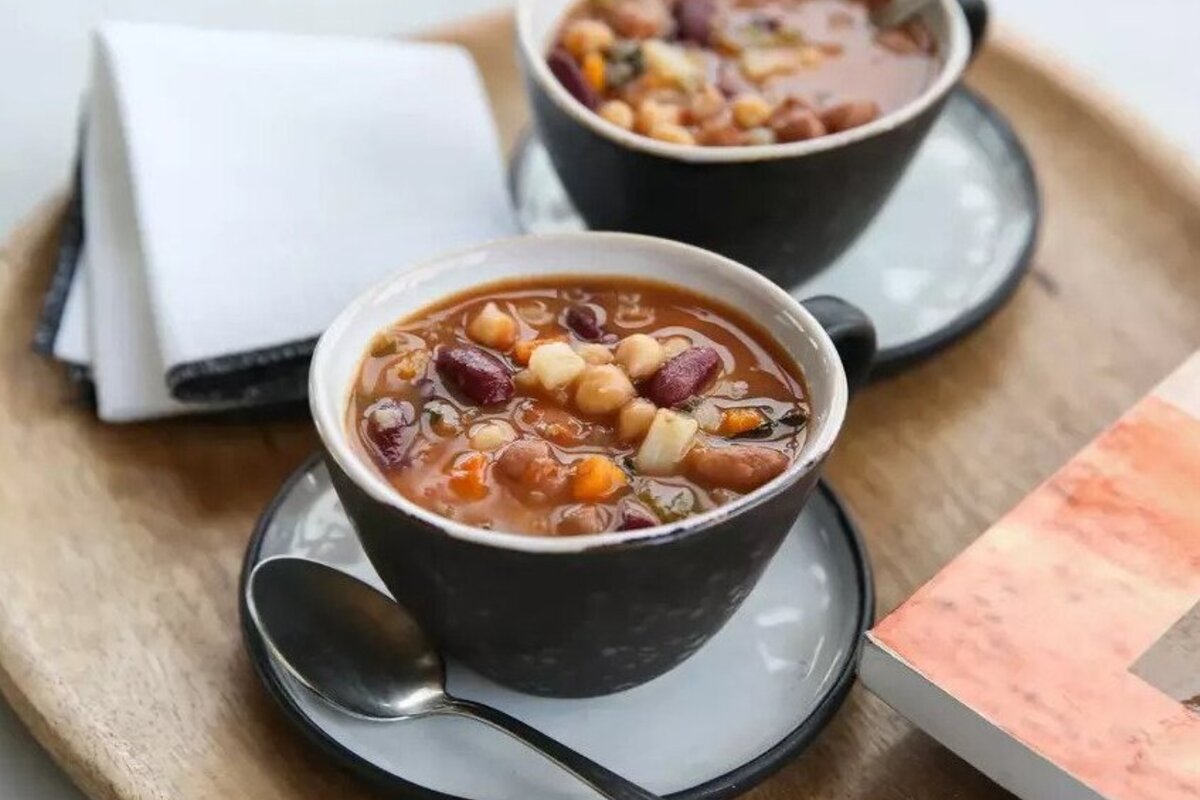 Two bowls of Italian three-bean minestrone soup served on a wooden tray with a spoon and folded napkin