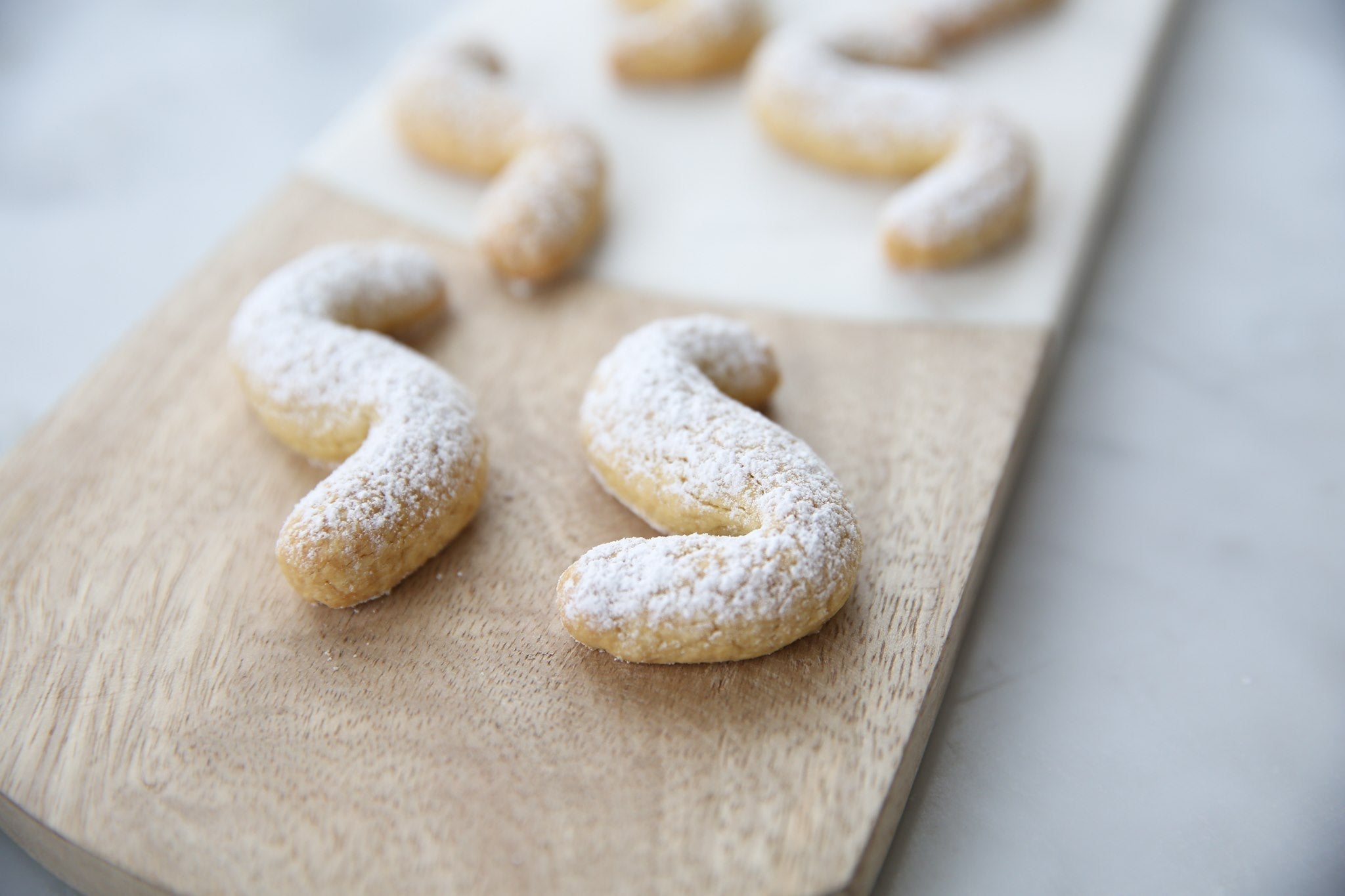 Close-up of two S-shaped Einkorn Italian shortbread cookies dusted with powdered sugar on a wooden serving board