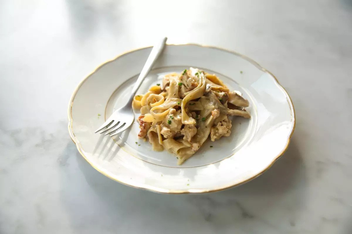 Creamy chicken and mushroom tagliatelle with gluten-free noodles served on a white plate with a fork on a marble surface