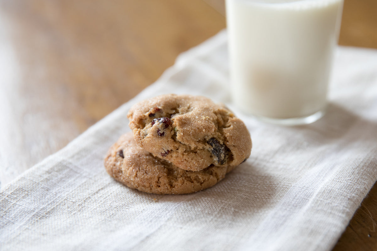 Close up of Einkorn cranberry pistachio cookies showing chewy texture and visible cranberries and pistachios with a glass of milk blurred in the background