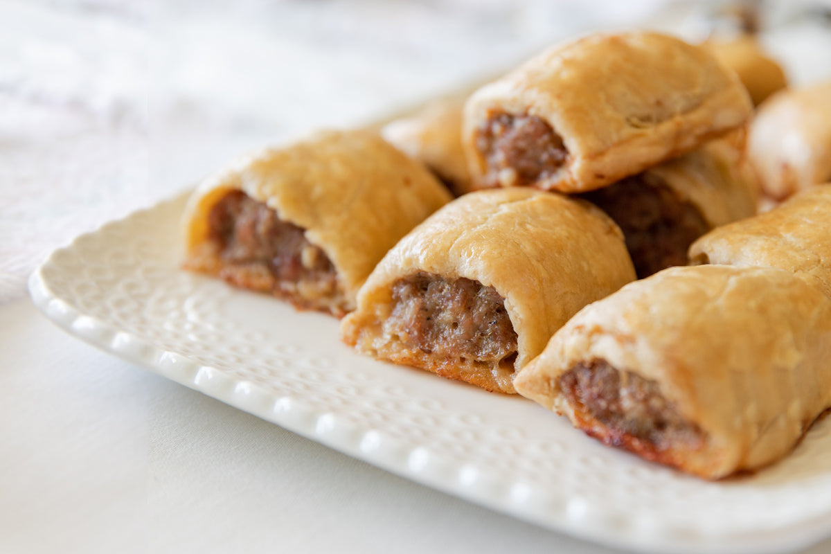 Close-up of einkorn sausage rolls showing golden flaky crust and savory sausage filling on a white textured ceramic platter