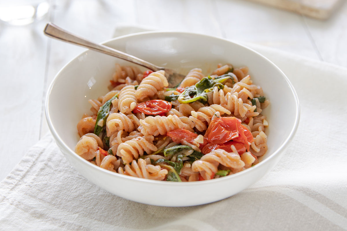 Bowl of gluten-free fusilli pasta tossed with garlicky broccoli rabe and blistered cherry tomatoes on a white linen napkin