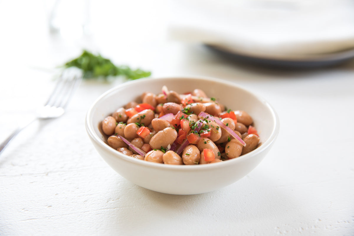Borlotti bean salad in a white bowl on a light table with diced red pepper, sliced red onion, and chopped parsley
