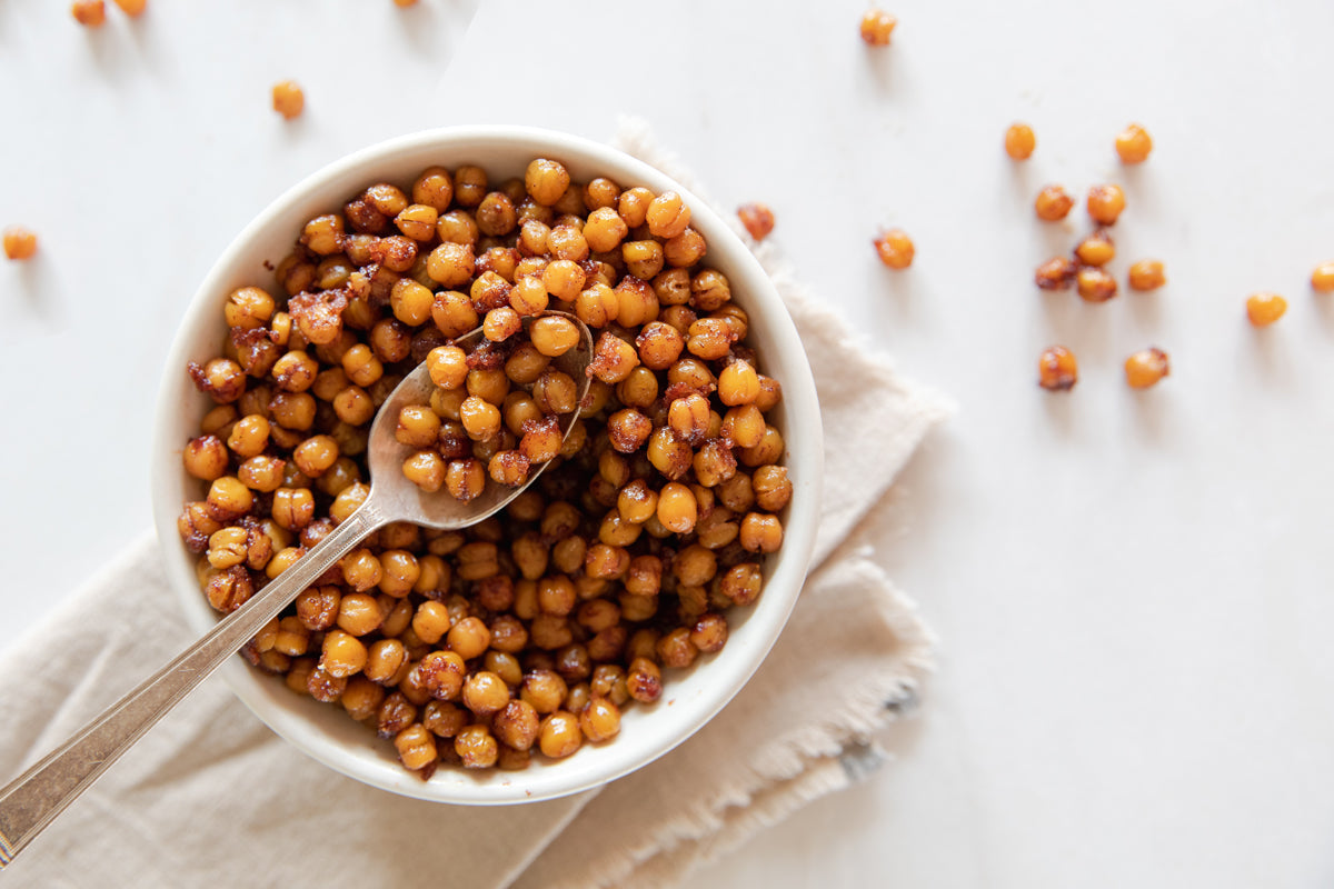 Bowl of cinnamon‑sugar roasted chickpeas with a spoon on a folded linen napkin and white background