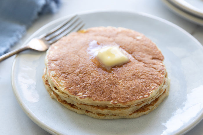 Top view of stacked Einkorn sourdough pancakes with a melting pat of butter on a white plate