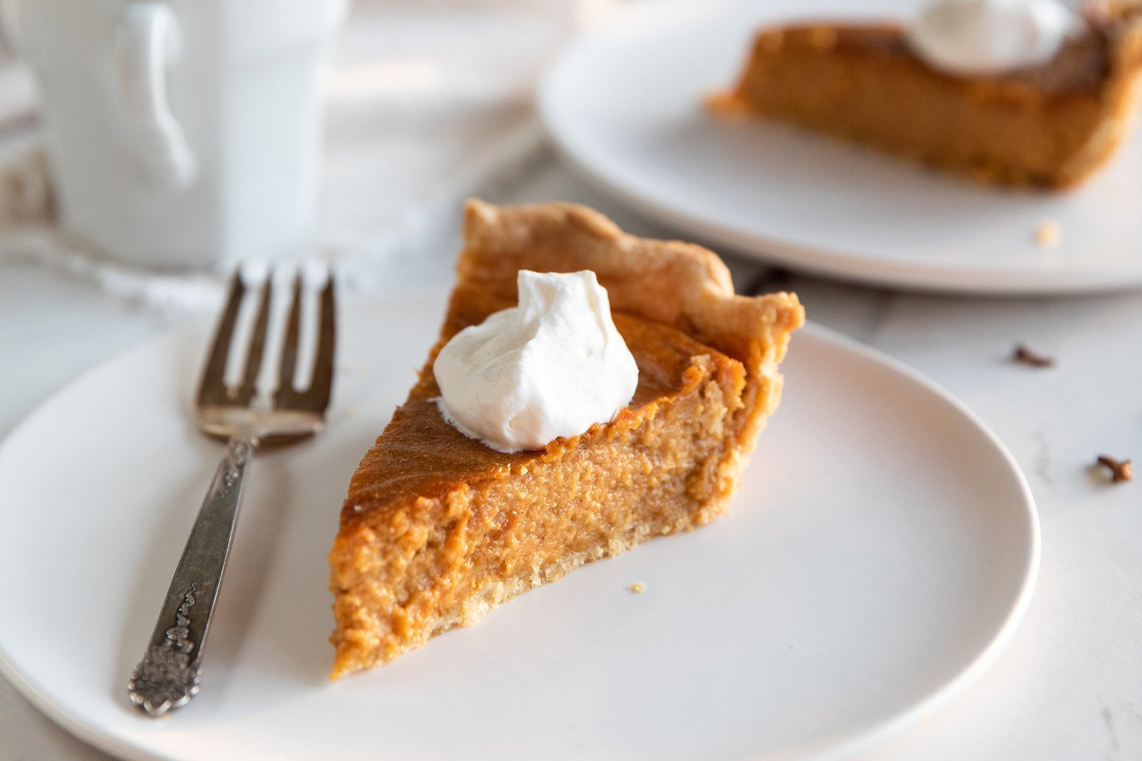 Three-quarter view of a slice of sweet potato pie with Einkorn crust showcasing creamy filling and whipped cream on a white plate with a fork