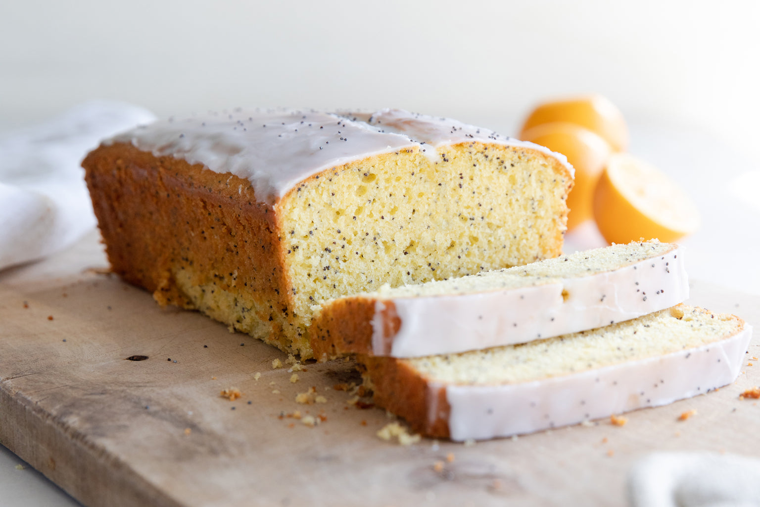 Three quarter view of sliced Einkorn lemon poppyseed loaf showcasing glazed top and poppy seeds on wooden cutting board