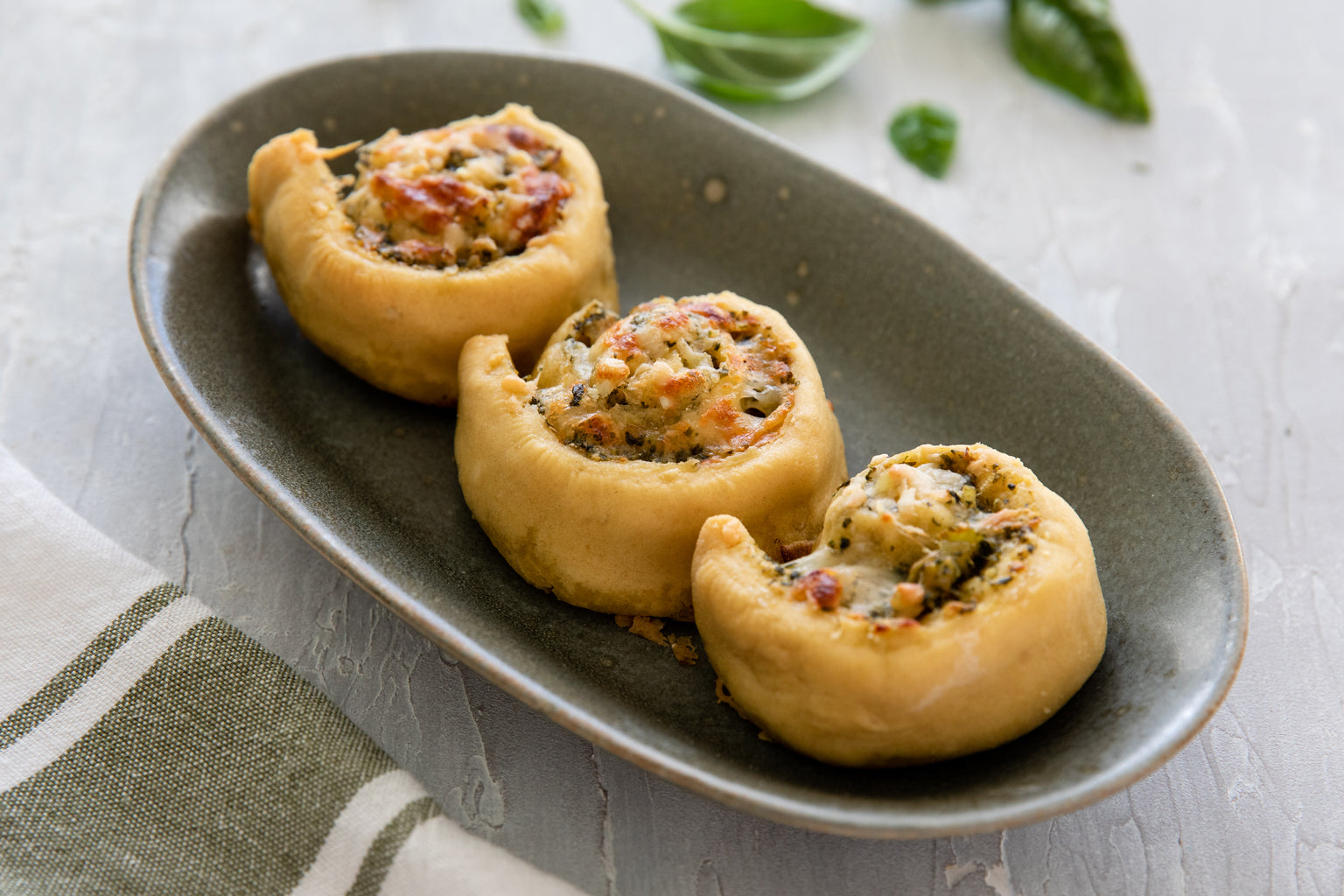 Three stuffed einkorn pizza spirals with cheesy leek and pesto served on a gray oval plate on a light textured tabletop
